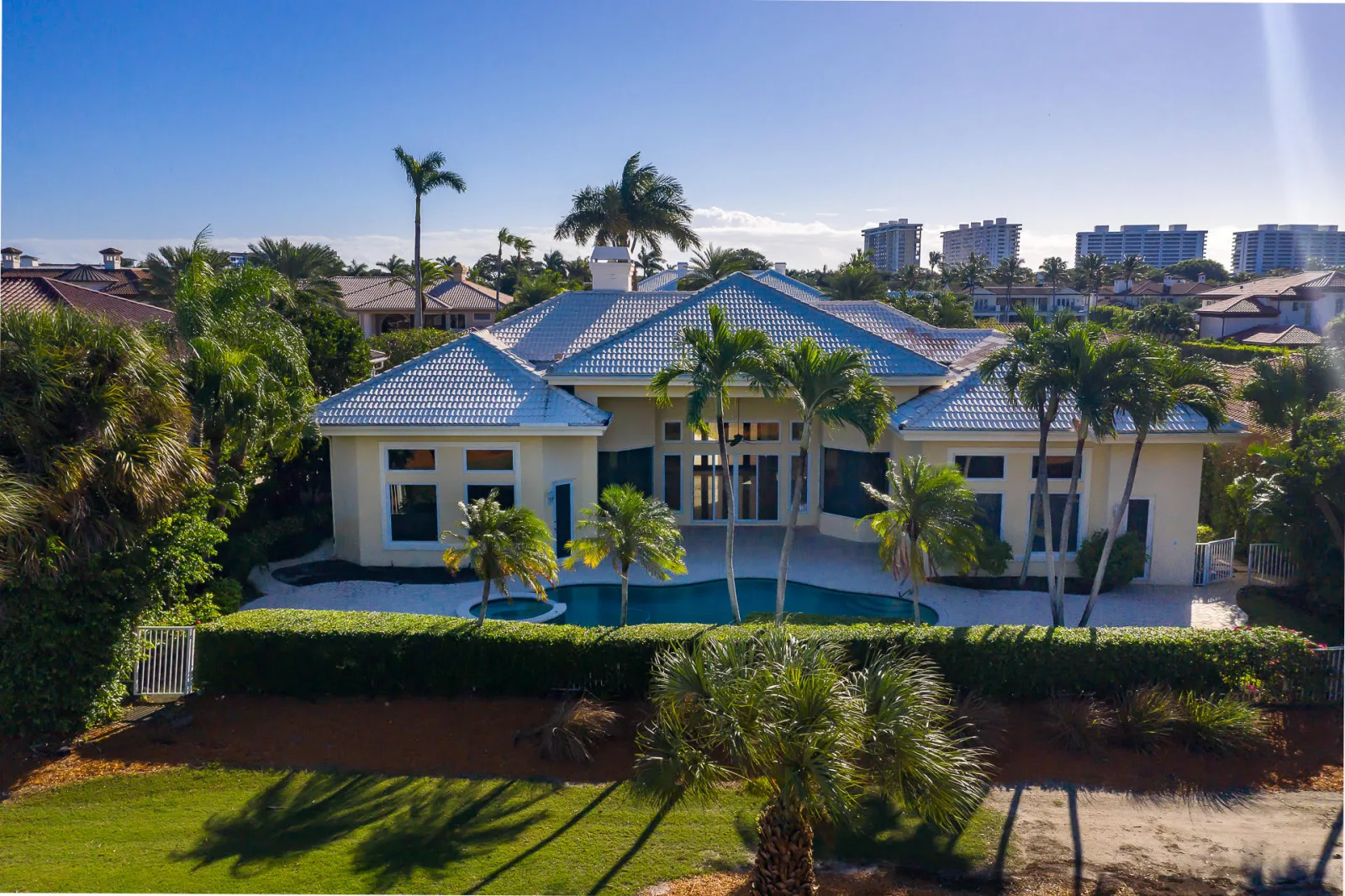 The rear elevation of 1521 Royal Palm Way, its free-form pool and covered terrace framed by mature palms, with the clipped hedge and golf course beyond