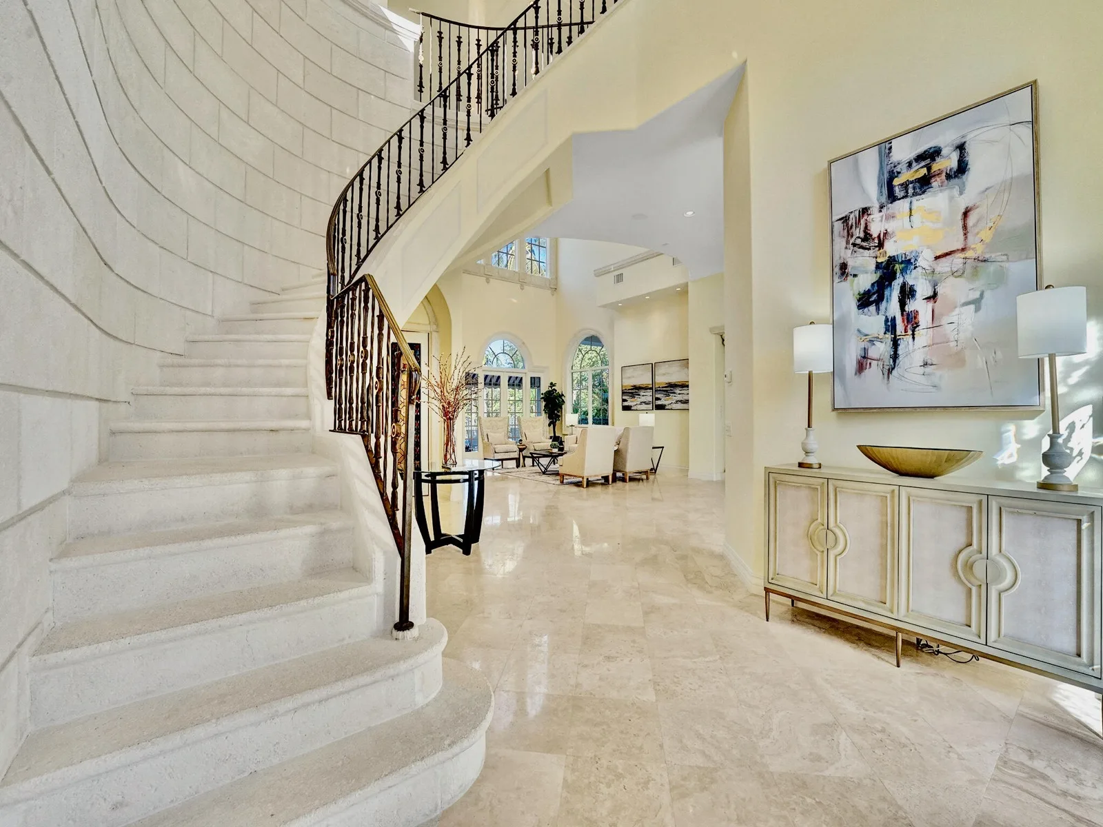 The curved stair at 422 Addison Park Lane, pale treads rising behind a wrought-iron balustrade above large squares of pale stone