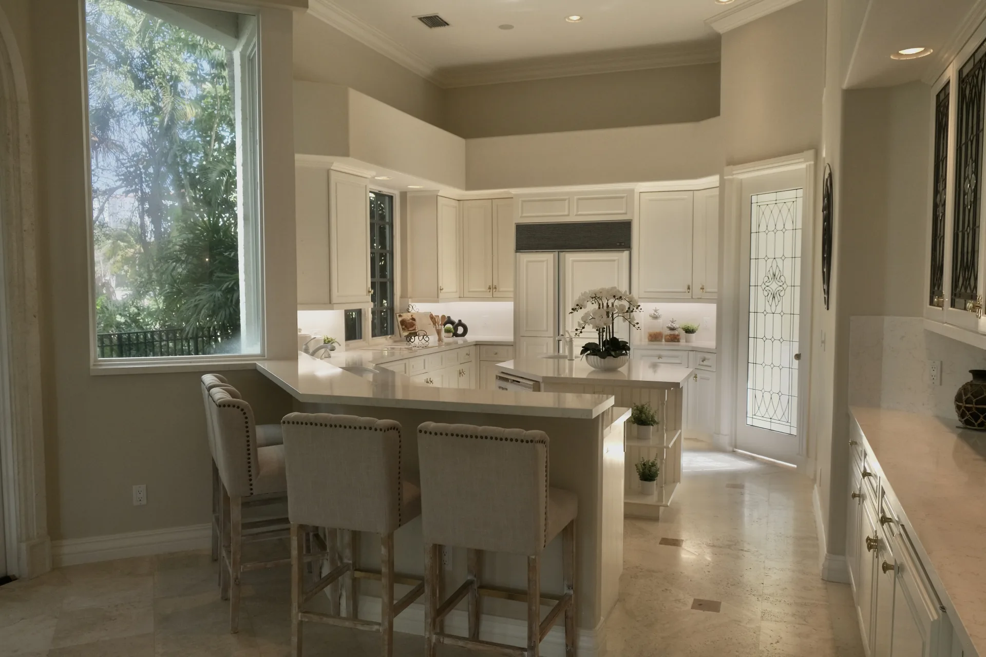 The kitchen at 422 Addison Park Lane, white cabinetry with leaded-glass doors around a peninsula and a separate island, a picture window looking out to the grounds