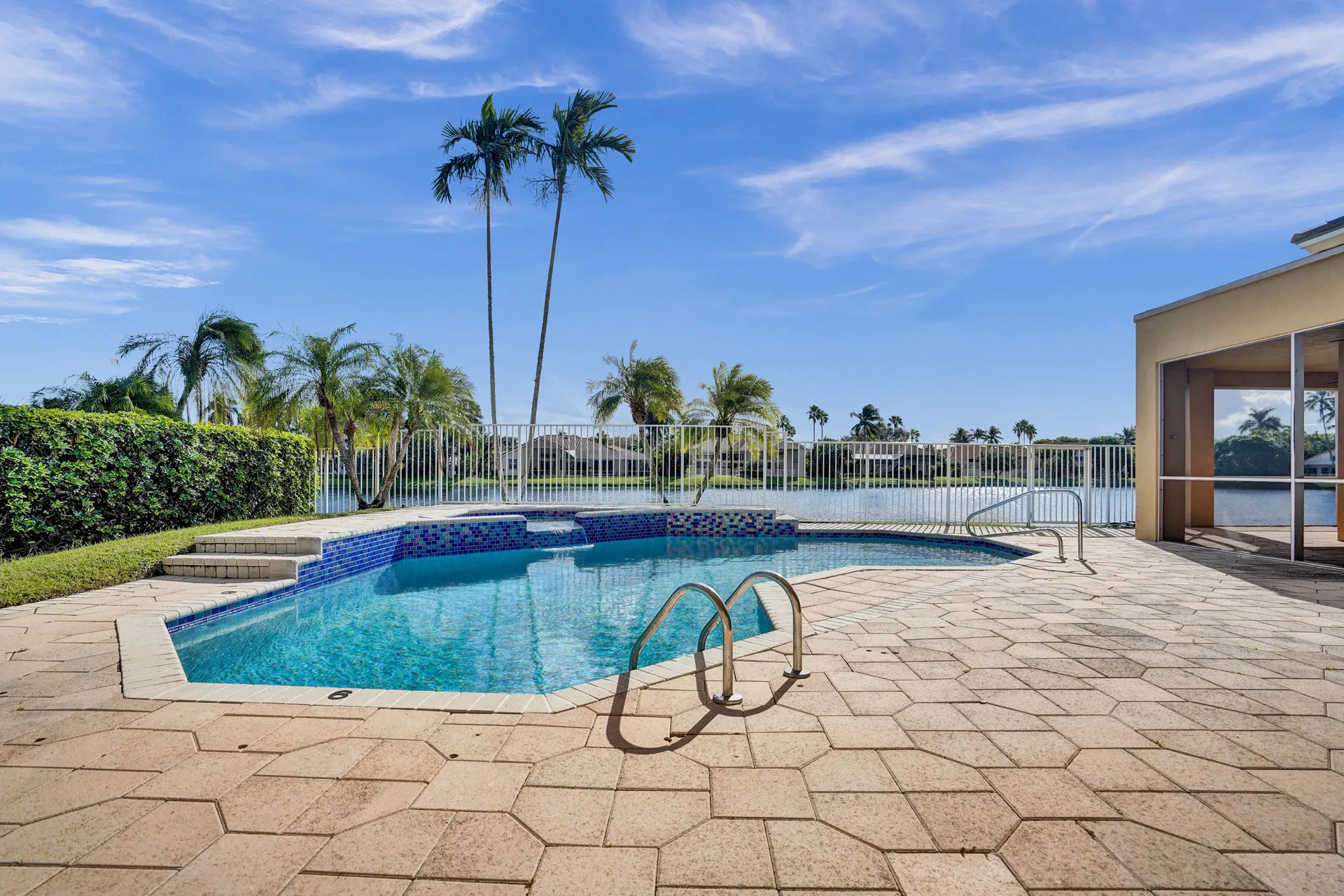 The pool and raised spa at 6543 Newport Lake Circle, edged in blue mosaic tile on fan-patterned pavers, with a white picket fence and the lake beyond