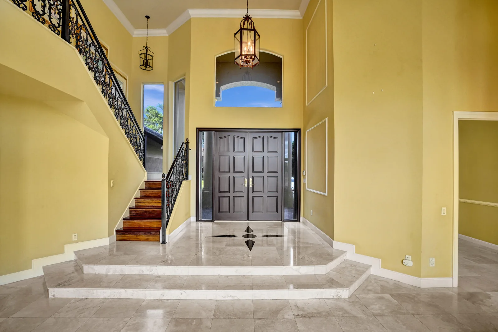 The two-storey foyer at 6543 Newport Lake Circle, the four-point compass star inlaid into the pale stone floor beneath a scrolling iron balustrade and two hanging lanterns