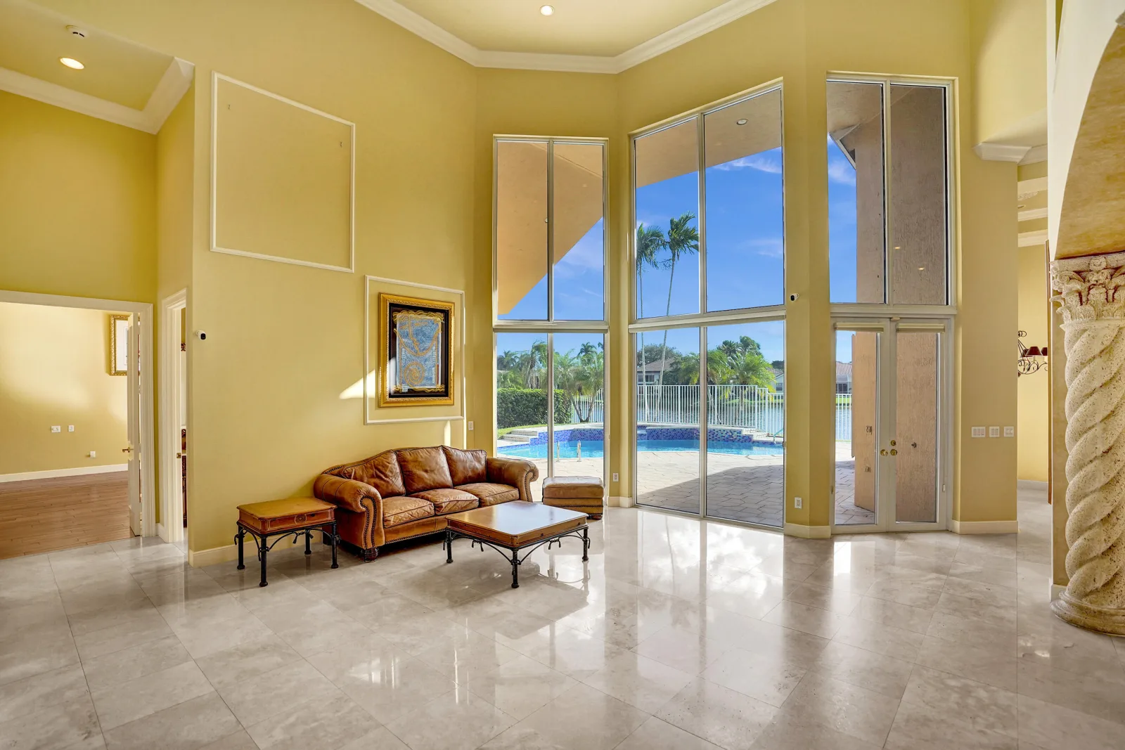 The double-height living room at 6543 Newport Lake Circle, its two-tier wall of glass opening onto the pool terrace with the lake beyond