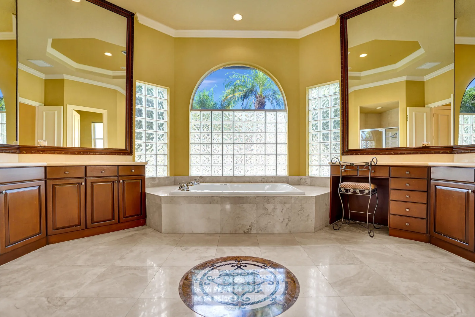 The primary bath at 6543 Newport Lake Circle, a soaking tub set beneath patterned glass block and an arched pane of clear glass, with a scrolled medallion inlaid into the stone floor