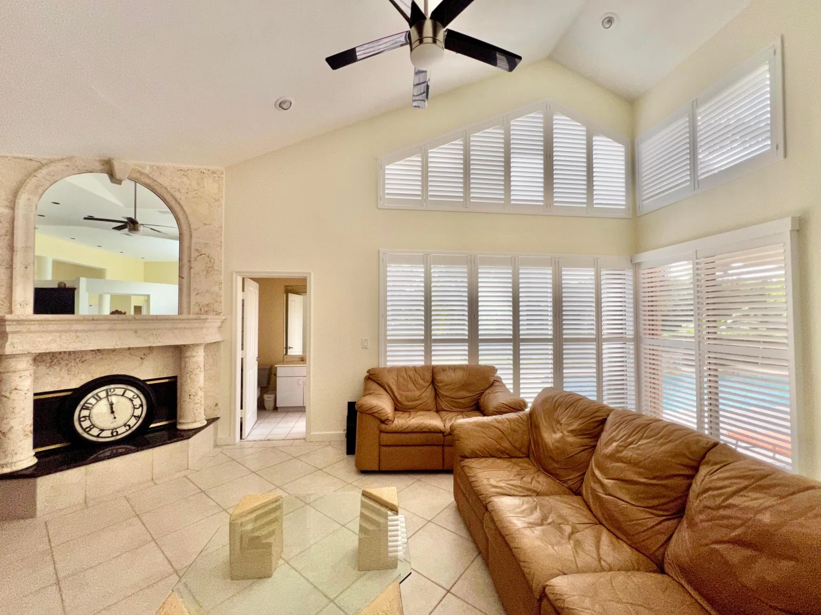 The family room at 6662 Newport Lake Circle, its ceiling climbing to a vaulted peak above a triangular shuttered window, with a pale stone fireplace framed by columns beneath a mirrored overmantel
