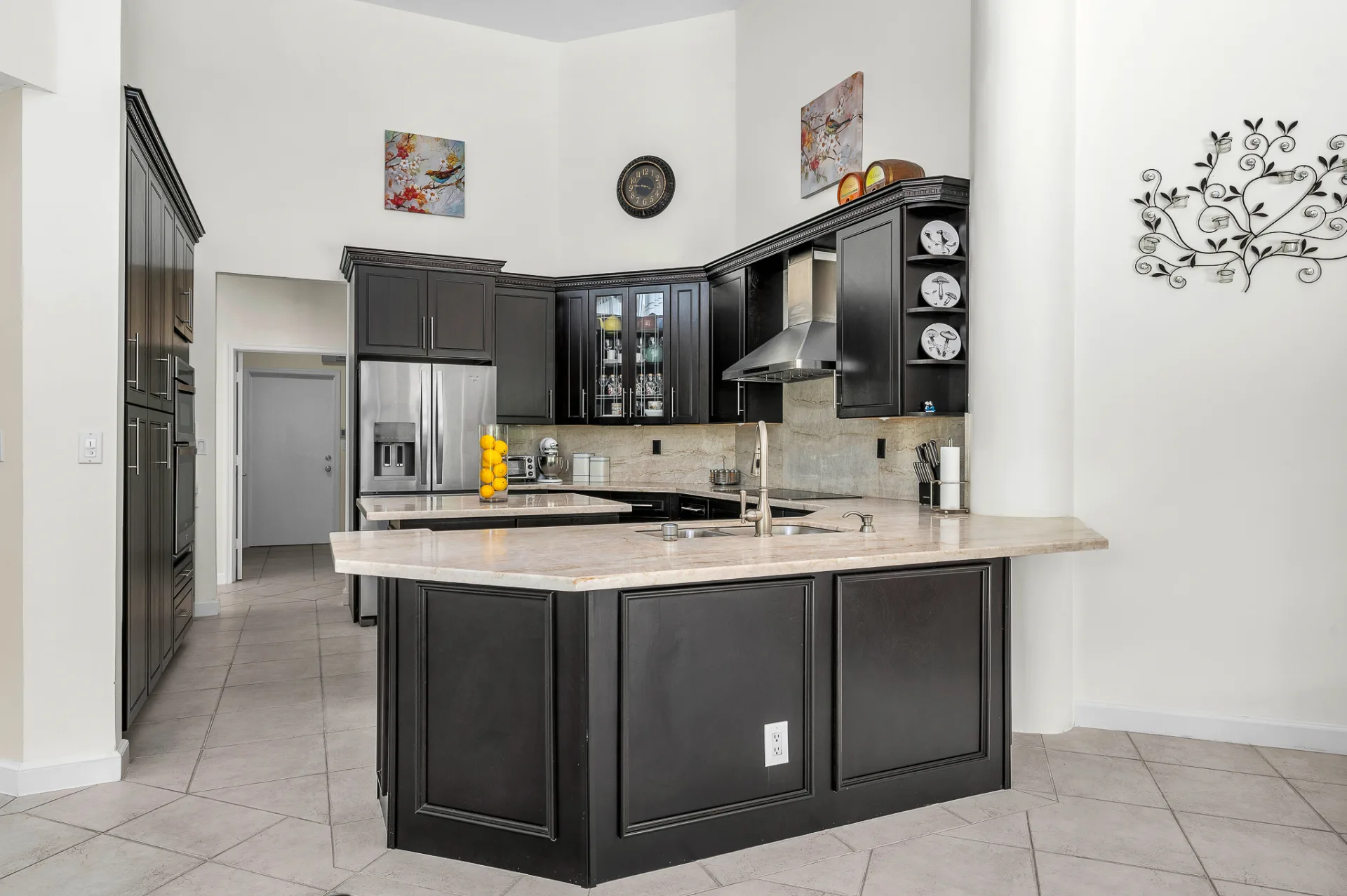 The kitchen at 6662 Newport Lake Circle, espresso cabinetry against white quartzite, an L-shaped peninsula with the double-bowl sink, and a stainless chimney hood above the cooktop