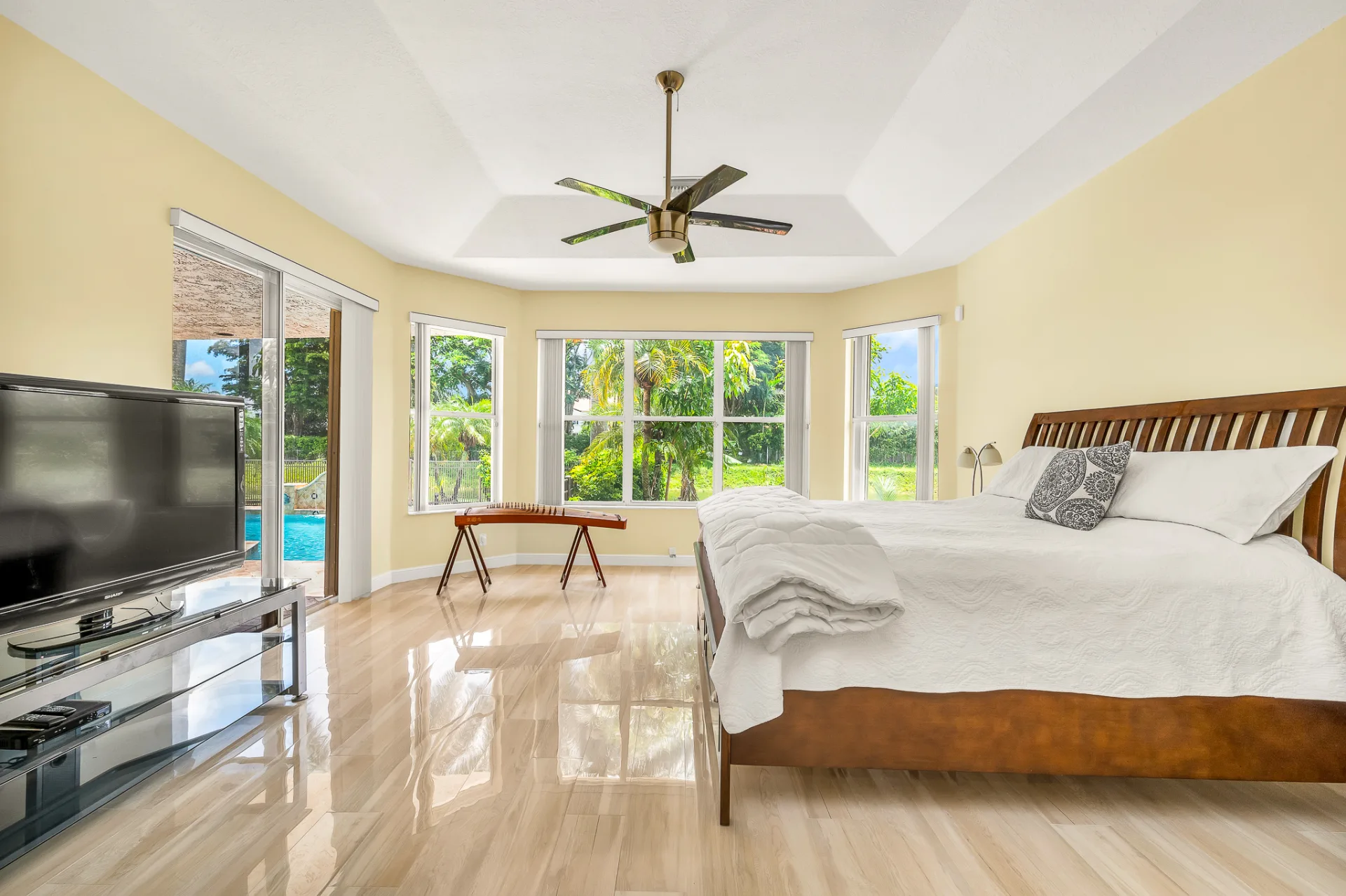The primary bedroom at 6662 Newport Lake Circle, sliding glass doors opening toward the pool beneath a stepped tray ceiling, with a three-window bay alongside
